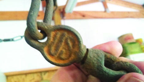 An antique chain swivel stamped with "US" being held up to the camera